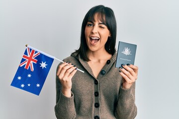 Young hispanic woman holding australian flag and passport winking looking at the camera with sexy...