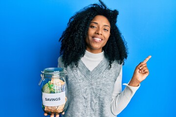 African american woman with afro hair holding savings jar with south african rands money smiling...