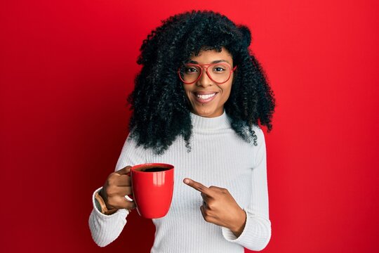 African american woman with afro hair holding coffee smiling happy pointing with hand and finger