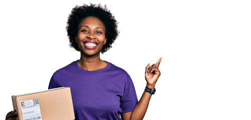 African american woman with afro hair holding delivery package smiling happy pointing with hand and...