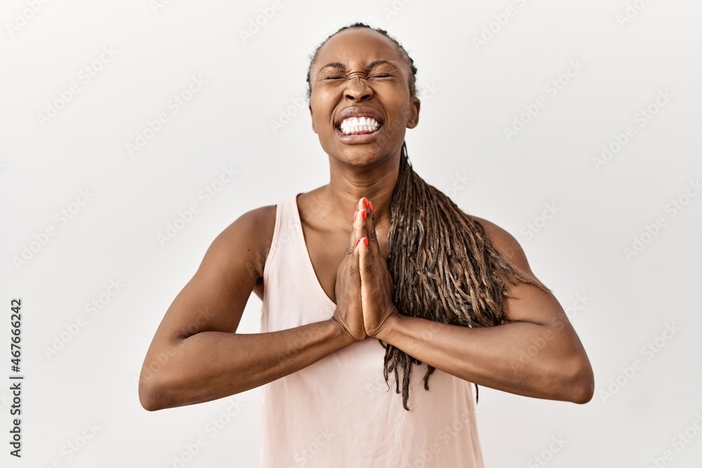 Poster black woman with braids standing over isolated background begging and praying with hands together wi