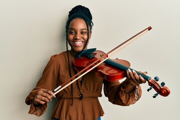 African american woman with braided hair playing violin winking looking at the camera with sexy expression, cheerful and happy face.