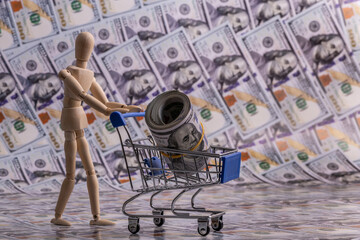 Wooden figurine of a symbolic person, a miniature shopping cart from a supermarket, symbolic home and 100 US dollar bills