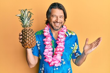 Middle age handsome man wearing hawaiian lei holding pineapple celebrating achievement with happy...