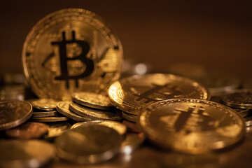 Golden coins scattered on surface with blurred bitcoin symbol on background