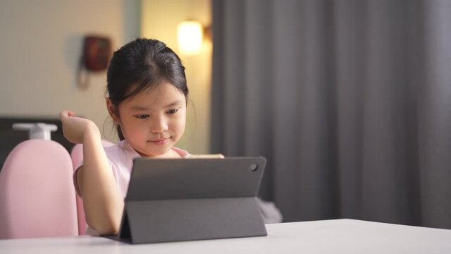 Asian child student or kid girl enjoy video calling talking or speaking with friend on computer tablet with phone in bedroom or person learning from home school and study online class on communication