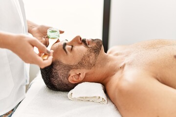 Obraz na płótnie Canvas Young hispanic man having facial mask treatment at beauty center