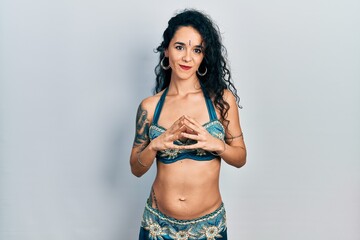 Young woman wearing bindi and traditional belly dance clothes hands together and fingers crossed smiling relaxed and cheerful. success and optimistic