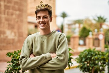 Young hispanic man smiling happy wearing gold king crown at the city.