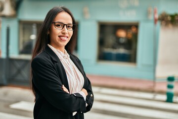 Young hispanic businesswoman smiling happy with arms crossed at the city.