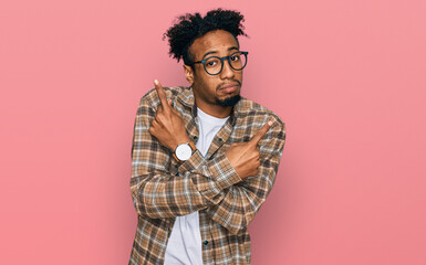 Young african american man with beard wearing casual clothes and glasses pointing to both sides with fingers, different direction disagree