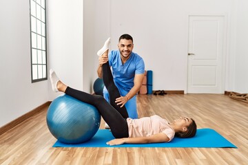 Latin man and woman wearing physiotherapist uniform having rehab session using fit ball at rehab...