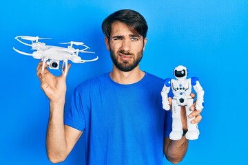 Fototapeta na wymiar Young hispanic man holding drone and robot toy clueless and confused expression. doubt concept.
