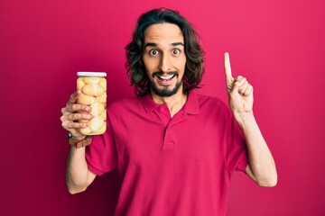 Young hispanic man holding bottle with boiled potatoes smiling with an idea or question pointing finger with happy face, number one