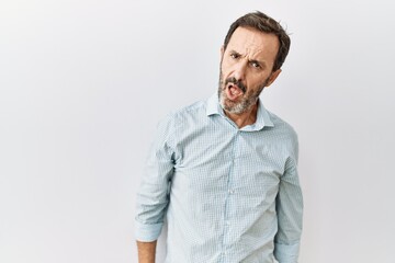 Middle age hispanic man with beard standing over isolated background in shock face, looking skeptical and sarcastic, surprised with open mouth