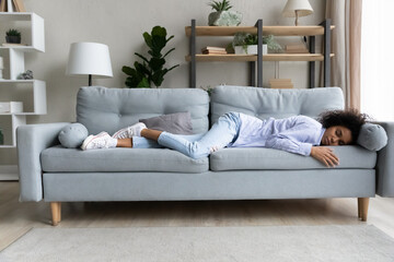 Full length relaxed African American woman sleeping on comfortable couch at home alone, beautiful young female resting with closed eyes, taking day nap, feeling tired and exhausted, lack of energy - obrazy, fototapety, plakaty