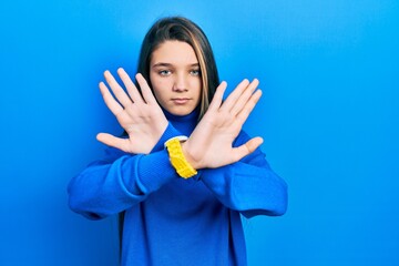 Young brunette girl wearing turtleneck sweater rejection expression crossing arms and palms doing negative sign, angry face