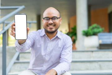 Bearded businessman smiling wearing glasses showing modern smartphone device typing text message in social media while sitting on stairs outdoor. Happy male spending free time in break of working.