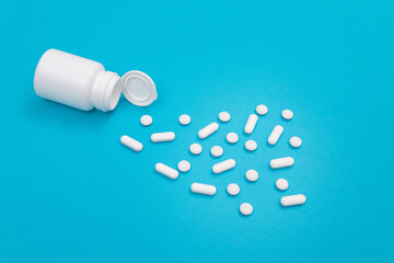 Global Pharmaceutical Industry and Medicinal Products - White Pills or Tablets Scattered from the Pill Container, Lying on Blue Background