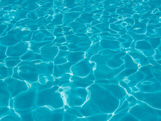 Background of blue transparent pool water with sun glare.