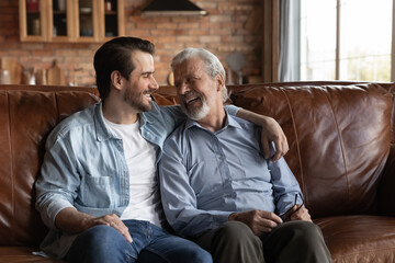 Bonding between generations. Happy elderly father adult son good friends relax on couch at home...