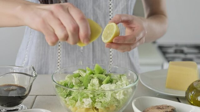 Woman adding lemon juice in salad. Process of preparing salad from tuna, cabbage, cheese and kiwi. Healthy food. Close-up in 4K, UHD