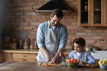 Helping daddy at kitchen. Tween child son learn to cook easy vegetarian salad watching young dad...