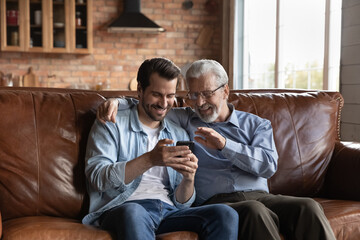 Making videocall. Excited retired male talk to grandkid by video call on smartphone with help of...