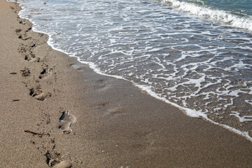 sea background surf with foam on sandy beach with footprints top view, horizontal.