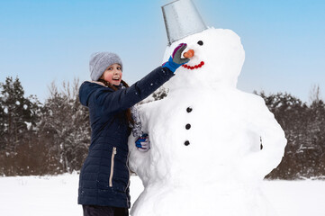 Cute girl makes  snowman on  winter day. Girl on a snow-covered field in the open air