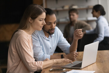 Happy concentrated two young employees colleagues coworkers working on online project on computer, discussing growth strategy or internet sales, sitting at table in coworking space office.