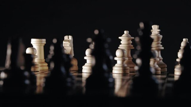  Dolly shot of chess pieces on wooden chessboard. Board strategy game. Teamwork, success business, intelligence sport concept. Black background.