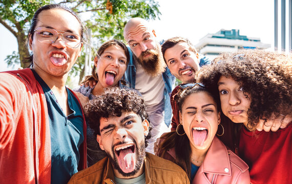 Multi cultural guys and girls taking funny selfie outdoor - Happy milenial life style concept by young multiracial friends having fun day together - Bright warm backlight filter - Focus on lower faces