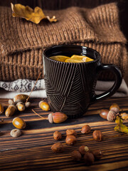 Autumn warming lemon tea on a wooden table with sweaters lying next to it and autumn tree leaves