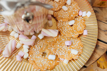 Cookies with sugar sprinkles are lying on golden plate, marshmello, wooden table, concept of...