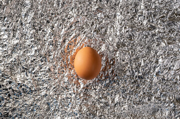1 brown chicken egg lies on crumpled metal foil. Contrast of colors and textures. Abstraction for Easter, healthy and wholesome food, living environment.