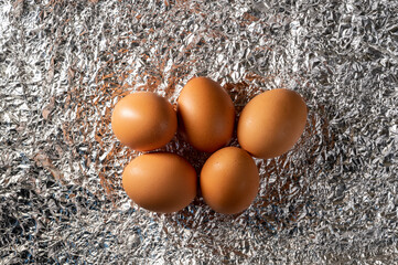 5 brown chicken eggs lies on crumpled metal foil. Contrast of colors and textures. Abstraction for Easter, healthy and wholesome food, living environment.