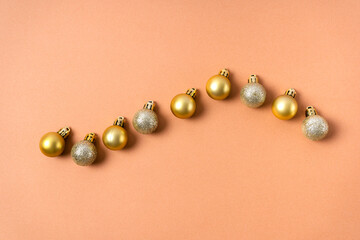Gold glittering balls on a Christmas tree are laid out in a row on a beige background. Christmas decorations