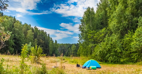 A summer landscape with grass, shrubs, trees, a tent and a blue sky with white clouds © Александр Коликов