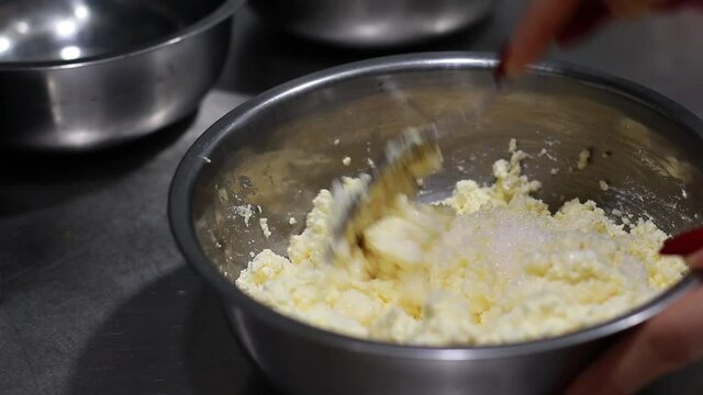 hand stirs cottage cheese in a bowl with a spoon, curd masswith shugar in a saucepan top view