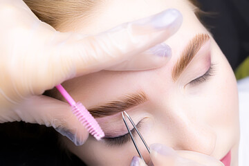 a close-up of the eyebrows of the model, the master holds in his hand a tweezer that removes excess...