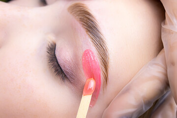 close-up of applying red wax to remove unwanted hairs from the lower contour of the model's eyebrows
