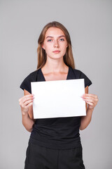 Fototapeta na wymiar Young girl holding a blank sheet of paper in her hands, isolated on gray background