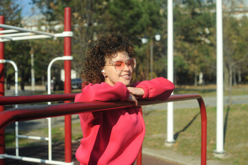 Obraz premium Cute curly hair woman in pink sportswear with headphones on the playground