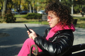 Obraz premium Curly hair woman in pink sportswear with headphones and mobile phone on the playground