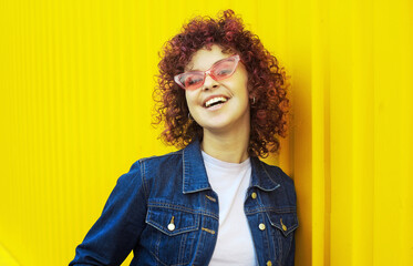 Happy curly haired woman in denim clothes on yellow background. Positive young woman outdoors....