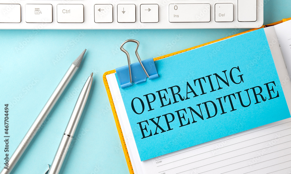Poster operating expendityre text on sticker on the blue background with pen and keyboard