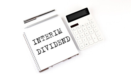 Notepad with text INTERIM DIVIDEND with calculator and pen. White background. Business concept