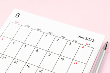 June 2022 calendar sheet with pen on pink background.