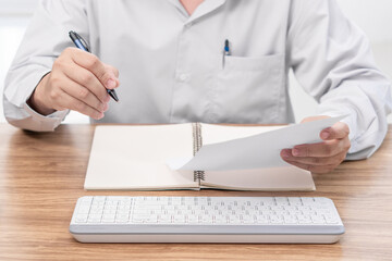 A man write on the paper check service list in office with repair part of car and laptop computer notebook keyboard on wood table